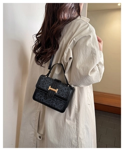 Close-up of black crossbody bag featuring CK monogram print and golden H-shaped hardware