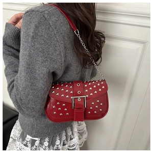 Close-up of a red punk shoulder bag with silver studs and metal chain on a model