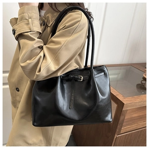 Detail of minimalist black leather tote bag featuring decorative belt and pin buckle accent