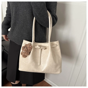 Detail of beige tote bag with buckle strap, long shoulder handles and a plush teddy charm