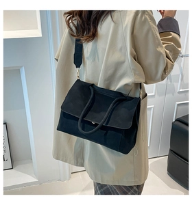 Detailed back view of a black matte leather tote bag with wide strap on a khaki coat