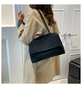 Side view of a vintage black flap shoulder bag worn with a beige trench coat
