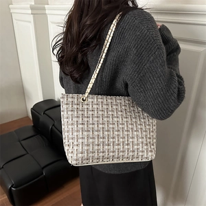 Brown tweed pattern tote bag with gold chain strap shown on model in minimalist room