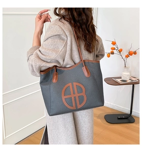 Detail of large woven canvas tote bag with brown leather trim and circular AB logo