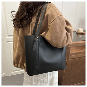 Detail van een grote zwarte kunstlederen tote bag met gouden gespen en smalle riem