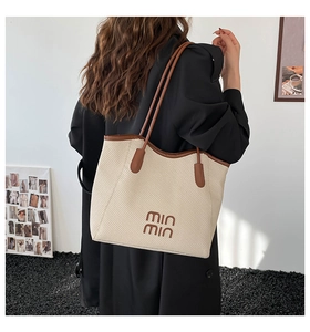 Detail of cream woven tote bag with brown leather trim and logo for daily commute