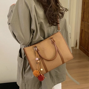 Brown woven tote bag with faux leather handles and colorful tassel charm on model