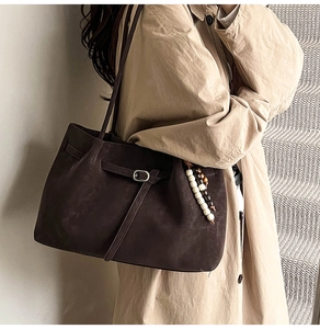 Detail of dark brown suede tote bag featuring a leather buckle and wooden bead charm