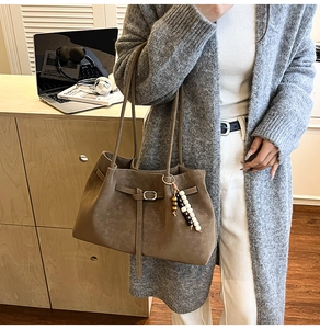 Detail of a dark brown suede tote bag with a beaded charm and slim metal buckle strap