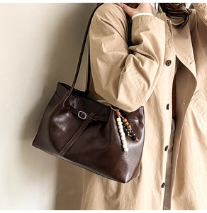Detail of dark brown leather tote with vintage strap buckle and bohemian beaded charm