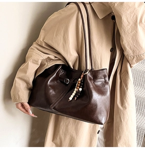 Detail of dark brown tote bag featuring beaded pendant and minimalist thin straps
