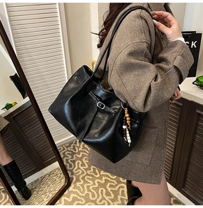 Detail of black faux leather tote bag with wooden bead charm on a checkered blazer