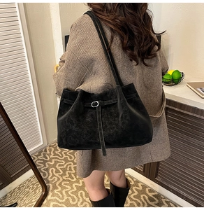 Detailed view of black matte suede shoulder bag with thin buckle on grey plaid blazer