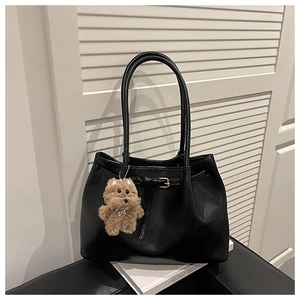 Detailed close-up of a black minimalist tote bag with a brown plush dog charm accessory