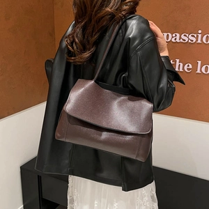 Vintage dark brown leather shoulder bag with wide strap worn by model in urban style