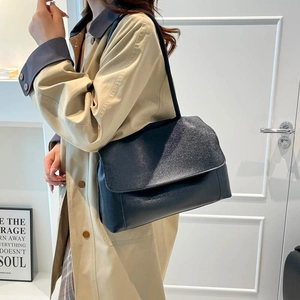 Minimalist black flap shoulder bag with textured finish worn with a beige trench coat