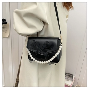Detail of black crossbody bag with chic chiffon bow and elegant pearl chain handle