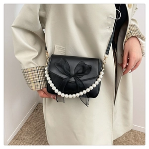 Close-up of black crossbody bag with mesh bow and decorative white pearl handle
