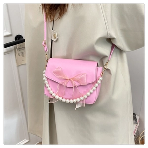 Detail of pink crossbody bag with organza bow and pearl chain on a female model
