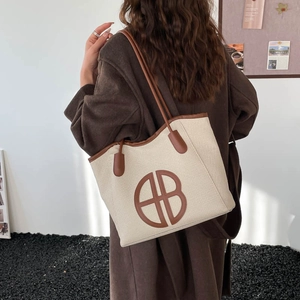 Large beige woven tote bag with brown leather trim and circular logo shown on model