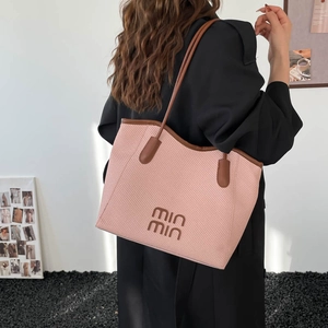 Pink woven tote bag with brown leather handles worn by model in minimalist studio