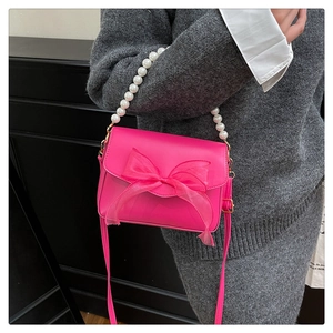 Detail view of pink bow purse with pearl chain and leather strap on grey dress