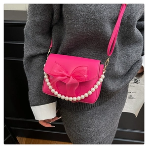 Close-up of bright pink shoulder bag featuring a large organza bow and pearl chain detail