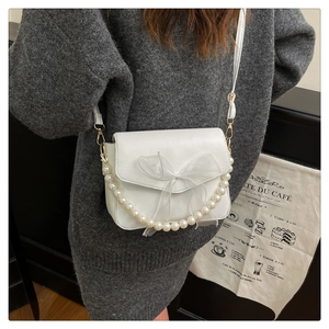 Close-up of white crossbody bag featuring organza bow and decorative pearl chain