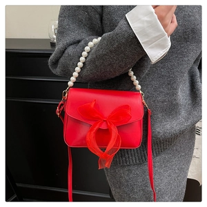 Detail of red crossbody bag with organza bow, pearl handle and smooth leather texture