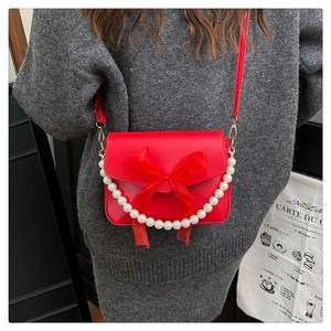 Detail of red crossbody bag featuring organza bow and white pearl chain strap accents