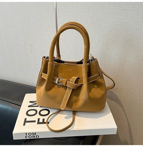 Detail of camel shoulder bag featuring contrast stitching and decorative belt buckle