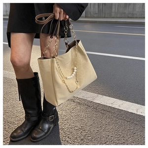Close-up of off-white tote bag featuring gold chain straps and decorative pearl flower charm