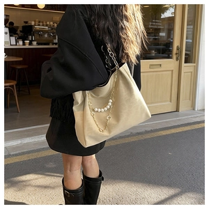 Detail of a large beige tote bag with elegant pearl and gold chain shoulder strap outdoors