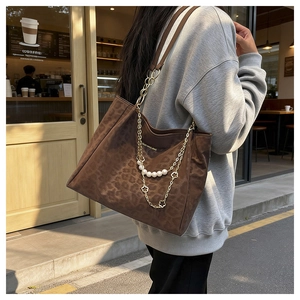 Detail of leopard print tote bag featuring metallic chain and pearl floral charms