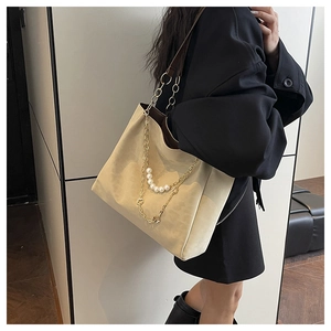 Detailed close-up of beige tote bag with gold chain and pearl strap on black coat