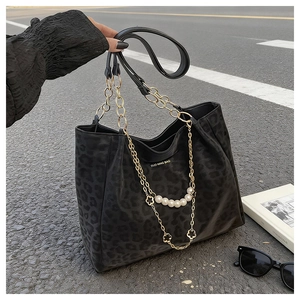 Detail of leopard print tote bag with gold chain, pearls and floral charms on asphalt