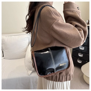 Detail of black glossy crossbody bag with brown trim and white stitching on a wool coat