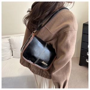 Detail of vintage black and brown leather crossbody bag with gold metal logo on the front