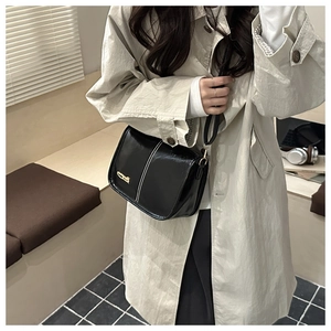 Detail of black glossy crossbody bag with white stitching and gold logo on model