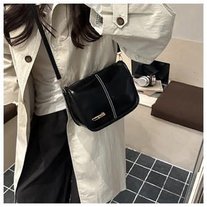Detail of black PU leather crossbody bag with white stitching and gold logo on beige coat
