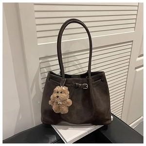 Detail of dark brown leather tote bag with decorative buckle and plush puppy charm