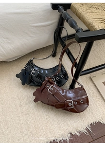 Detail of half-moon underarm bags in black and brown faux leather with buckle straps