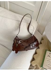 Detail of a brown crescent shoulder bag with metallic eyelets and floral charm on a sofa