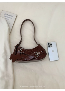 Detail of dark brown glossy leather baguette bag with metal buckles and phone for scale