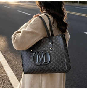 Detail of black tote bag with embossed M monogram pattern and golden rivet leather handles