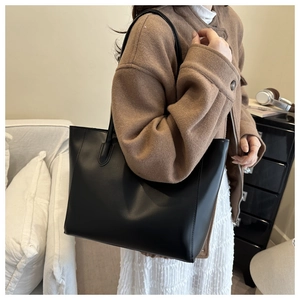 Minimalist black tote bag in matte leather worn by model with brown wool coat