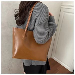 Brown leather tote bag detail showing slender shoulder strap and premium matte texture