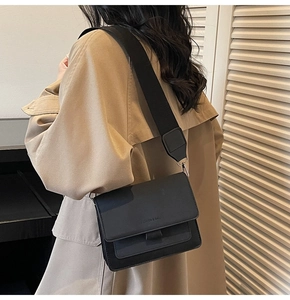 Close-up of small black leather crossbody bag with wide shoulder strap worn by a model
