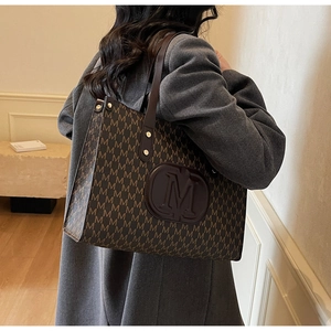 Detail of vintage tote bag with M-letter pattern and leather strap with rivet reinforcement
