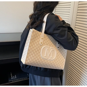 Detailed view of cream tote bag with repetitive M letter pattern and embossed M logo
